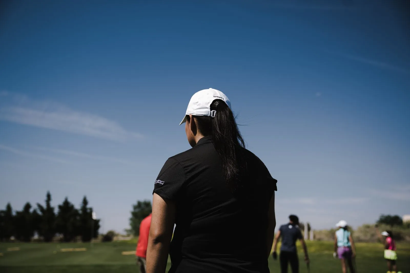 A woman golfer is focused on the golf course on a sunny day, ready to swing during a sports competition.